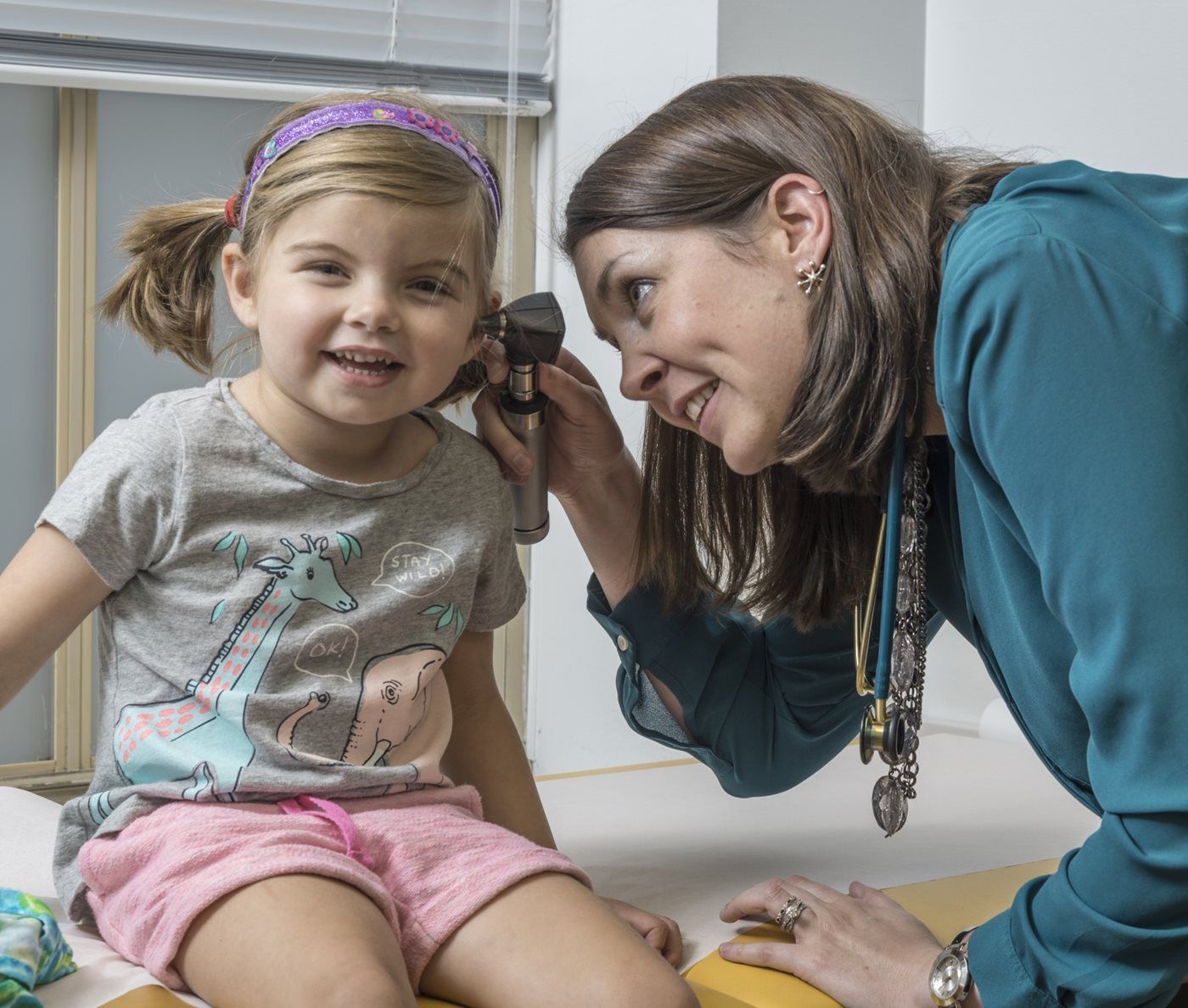A woman is listening to a little girl 's ear with a magnifying glass.