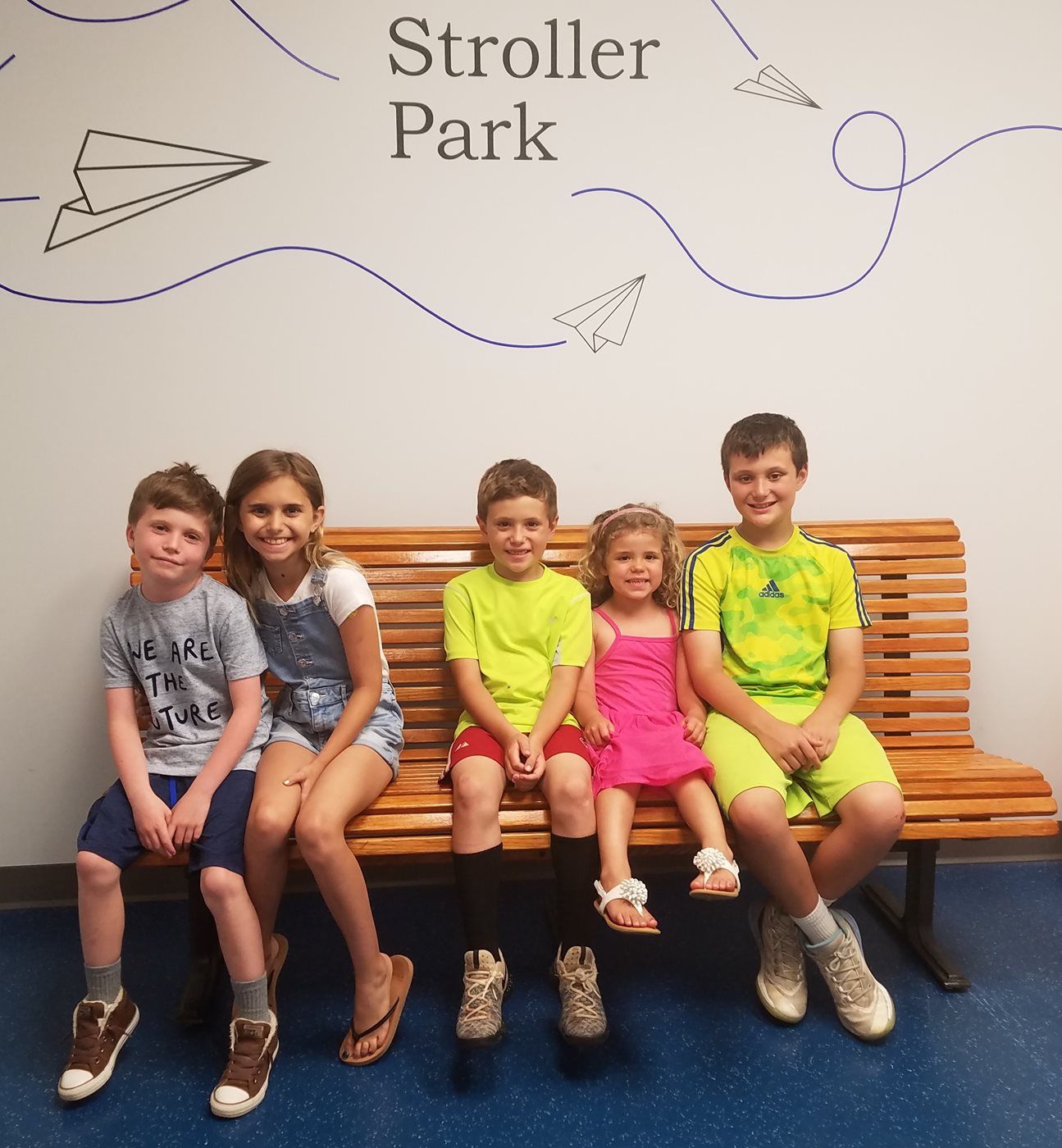 A group of children are sitting on a bench under a sign that says stroller park