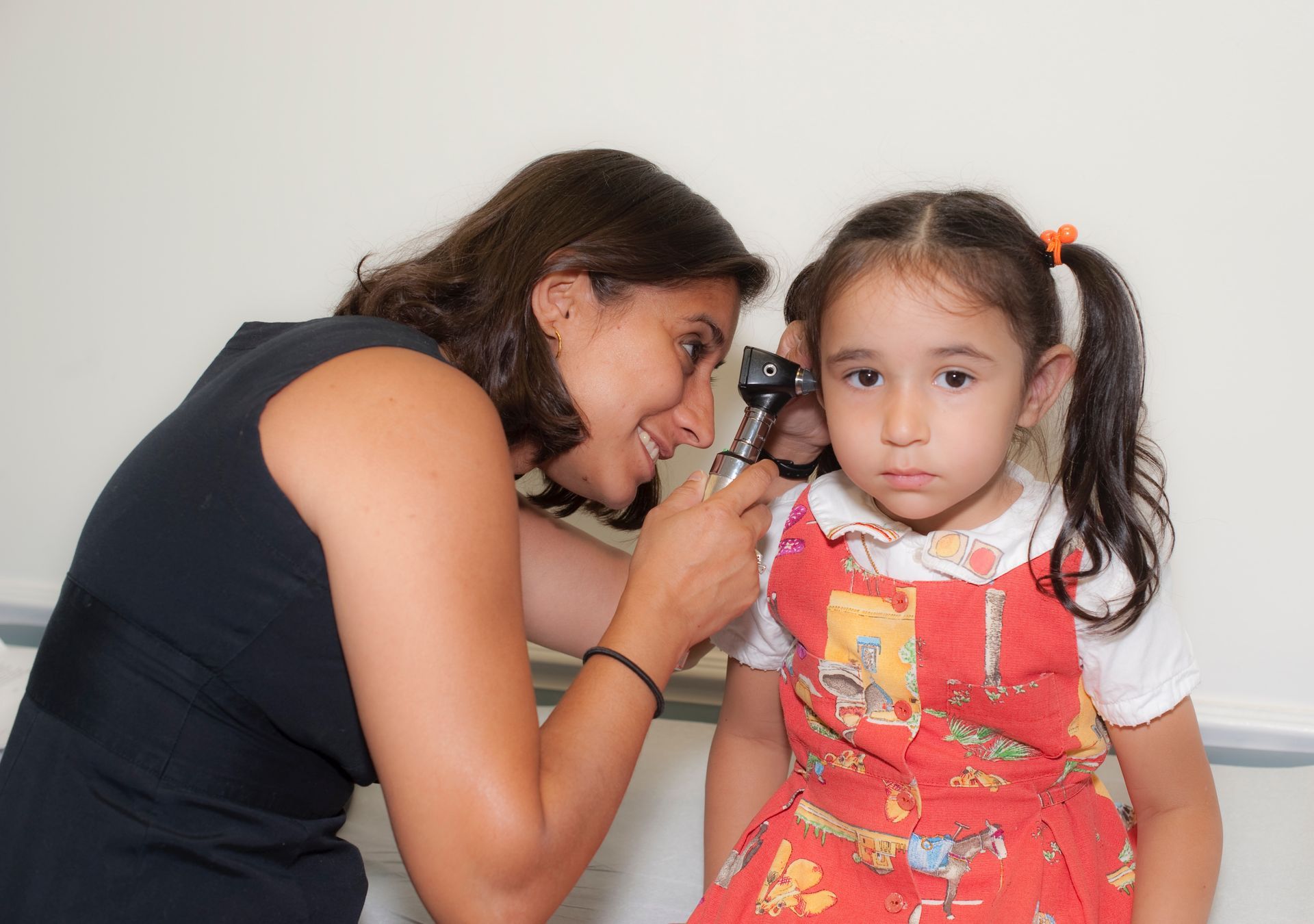A pediatrician is examining a girl using a otoscope