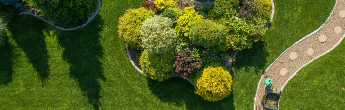 Overhead view of a green park with a stone path winding through the grass and colorful plants.