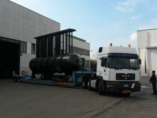 Un camion bianco che traina un grande serbatoio cilindrico nero in un'area industriale.