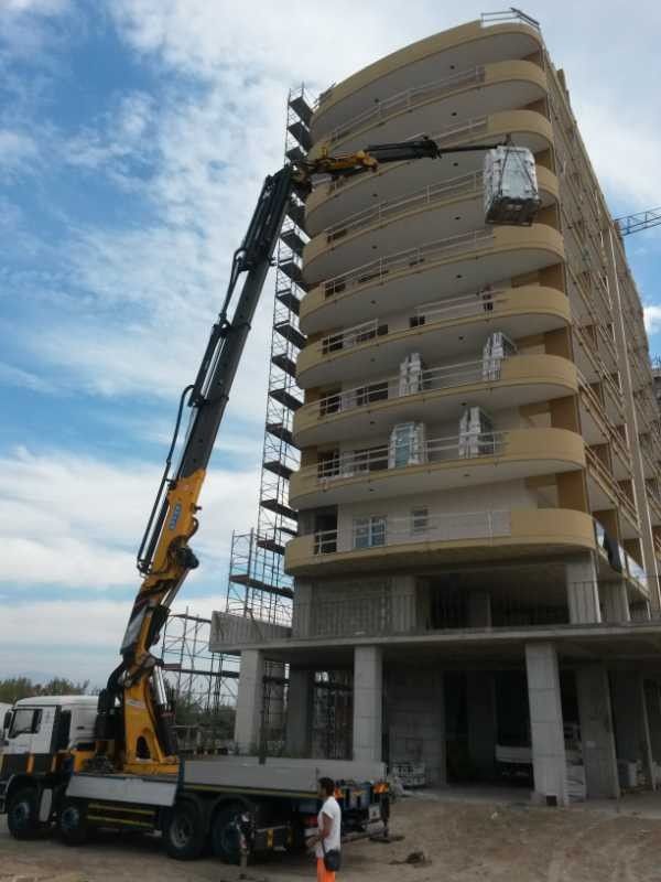 Una gru da cantiere solleva materiali accanto a un edificio beige a più piani in costruzione.