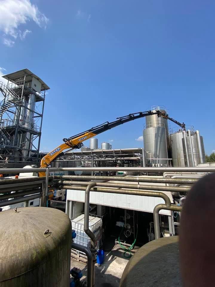 Impianto industriale con tubature, silos e una gru sotto un cielo azzurro limpido.