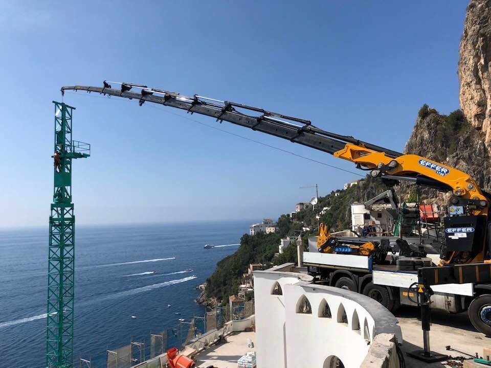 Gru da costruzione che si protende sulla scogliera a picco sull'oceano blu e su una strada costiera.
