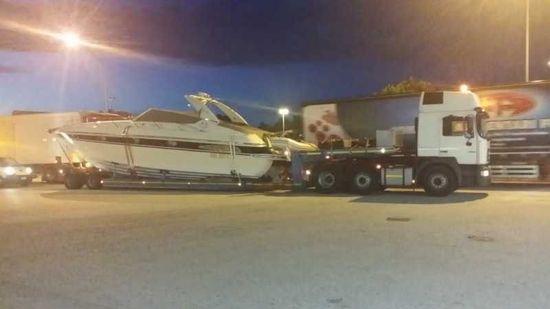 Motoscafo bianco su rimorchio agganciato a un camion bianco, di notte in un parcheggio.