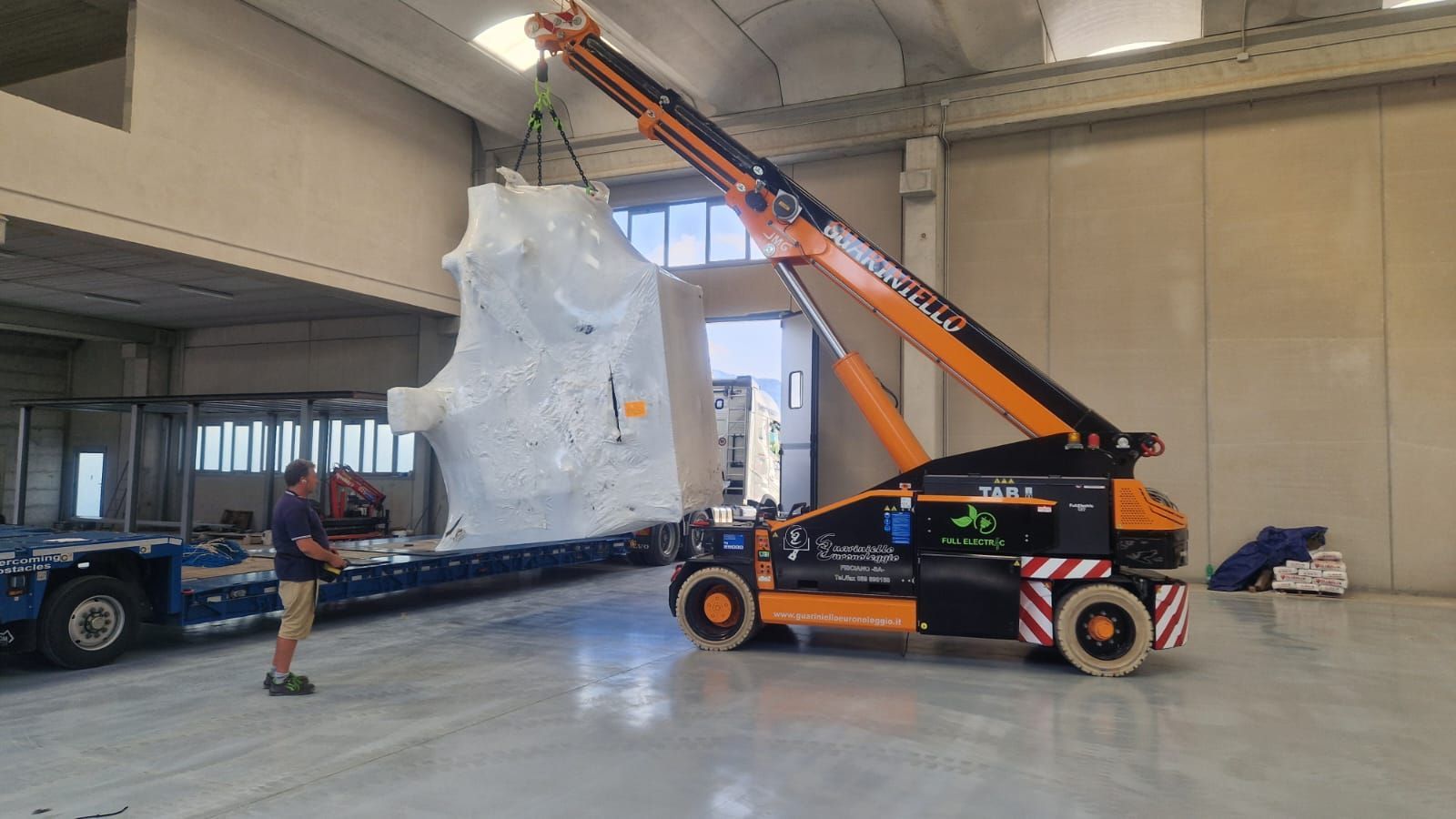 Carrello elevatore arancione che solleva un grande pallet imballato in un'area di carico del magazzino.