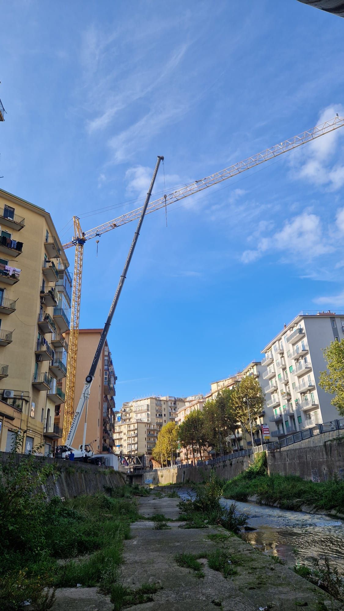 Un canale urbano tra palazzi residenziali in costruzione, con gru che si stagliano contro un cielo azzurro.