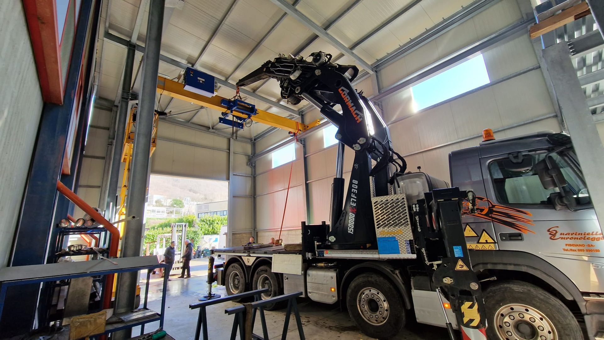 Attrezzatura di sollevamento con gru montata su camion all'interno di una baia di carico di un magazzino.