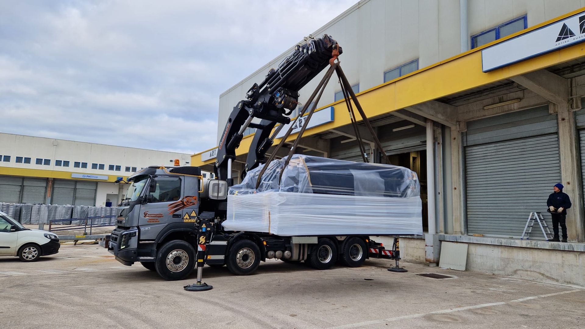 Un camion con gru nero scarica un veicolo imballato all'esterno della banchina di carico di un magazzino.