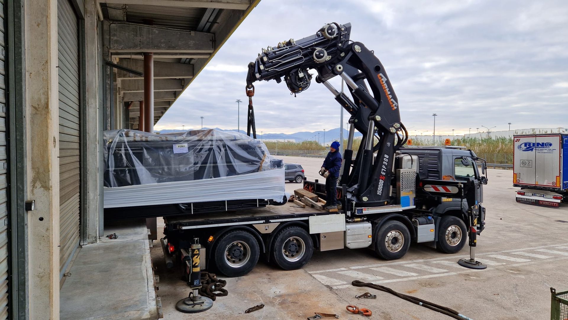Una gru per carichi pesanti carica un camion imballato su un rimorchio a pianale in un'area industriale.