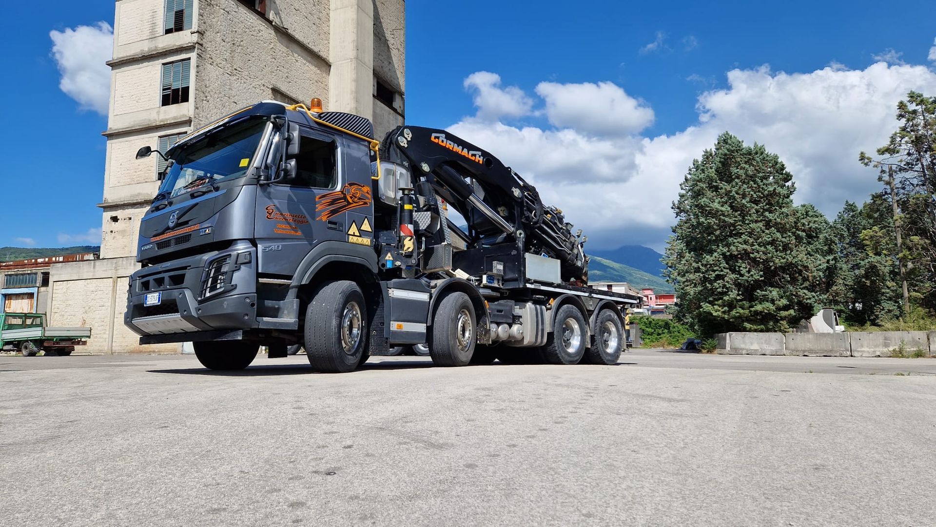 Un camion della spazzatura blu parcheggiato accanto a un edificio in pietra sotto un cielo soleggiato.