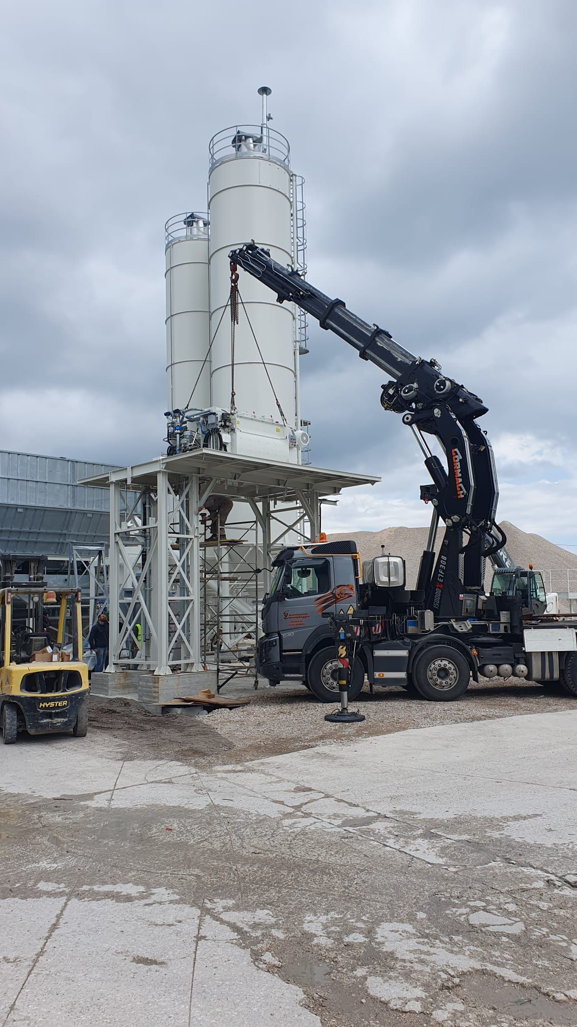 Un'autobetoniera con pompa versa il calcestruzzo in un alto silo bianco in un cantiere edile sotto un cielo nuvoloso.