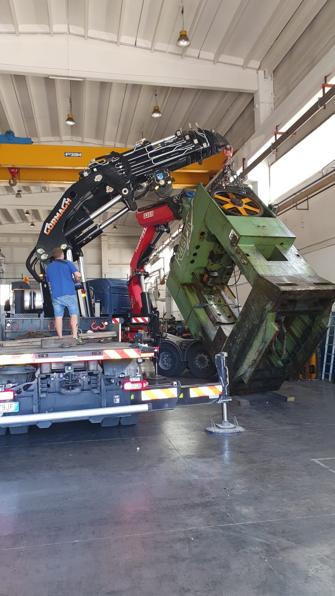 Un carro attrezzi solleva la cabina di un camion verde all'interno di un garage, con due operai nelle vicinanze.
