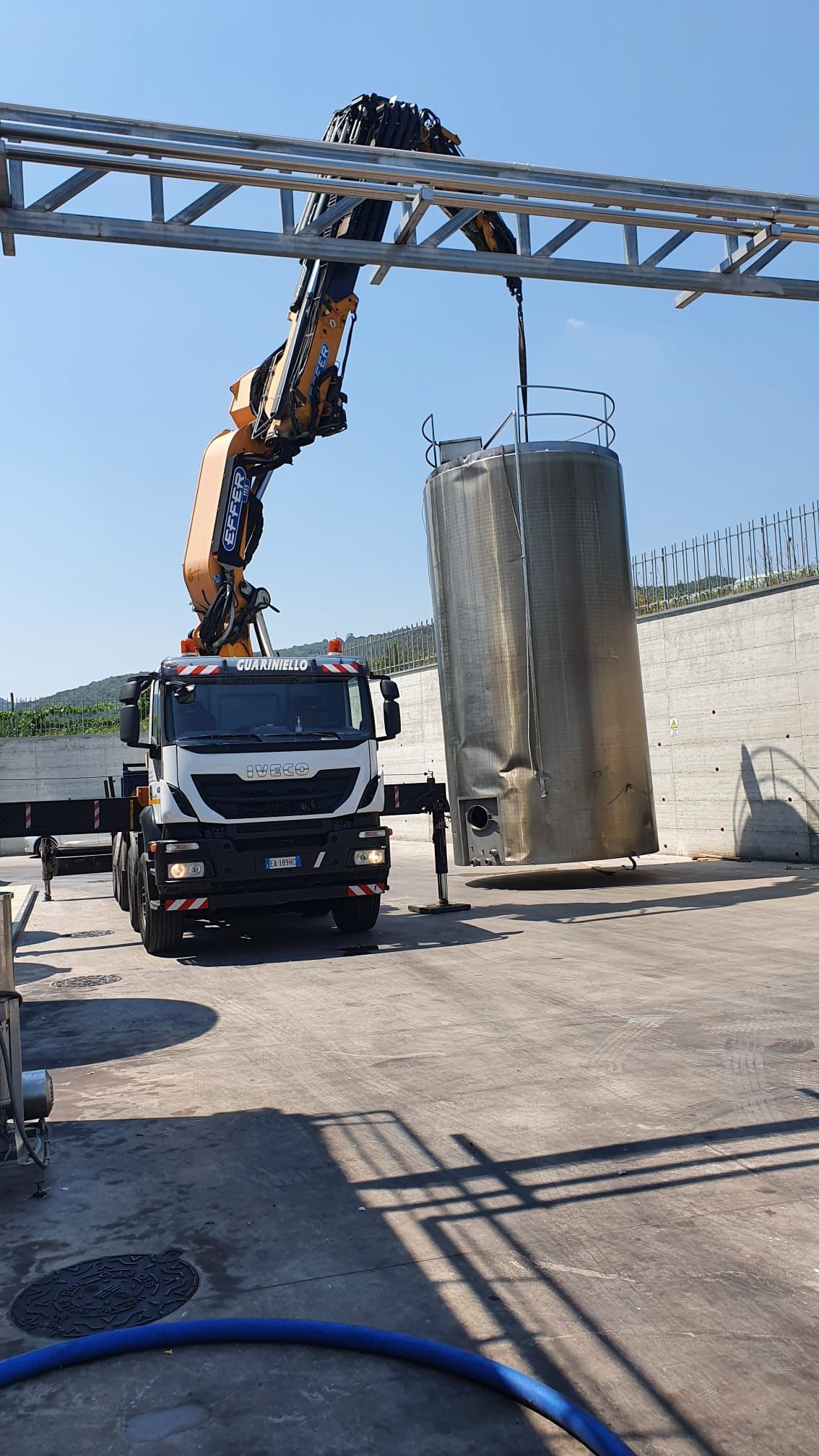Un camion con gru solleva un grande cilindro di cemento in un cantiere all'aperto.