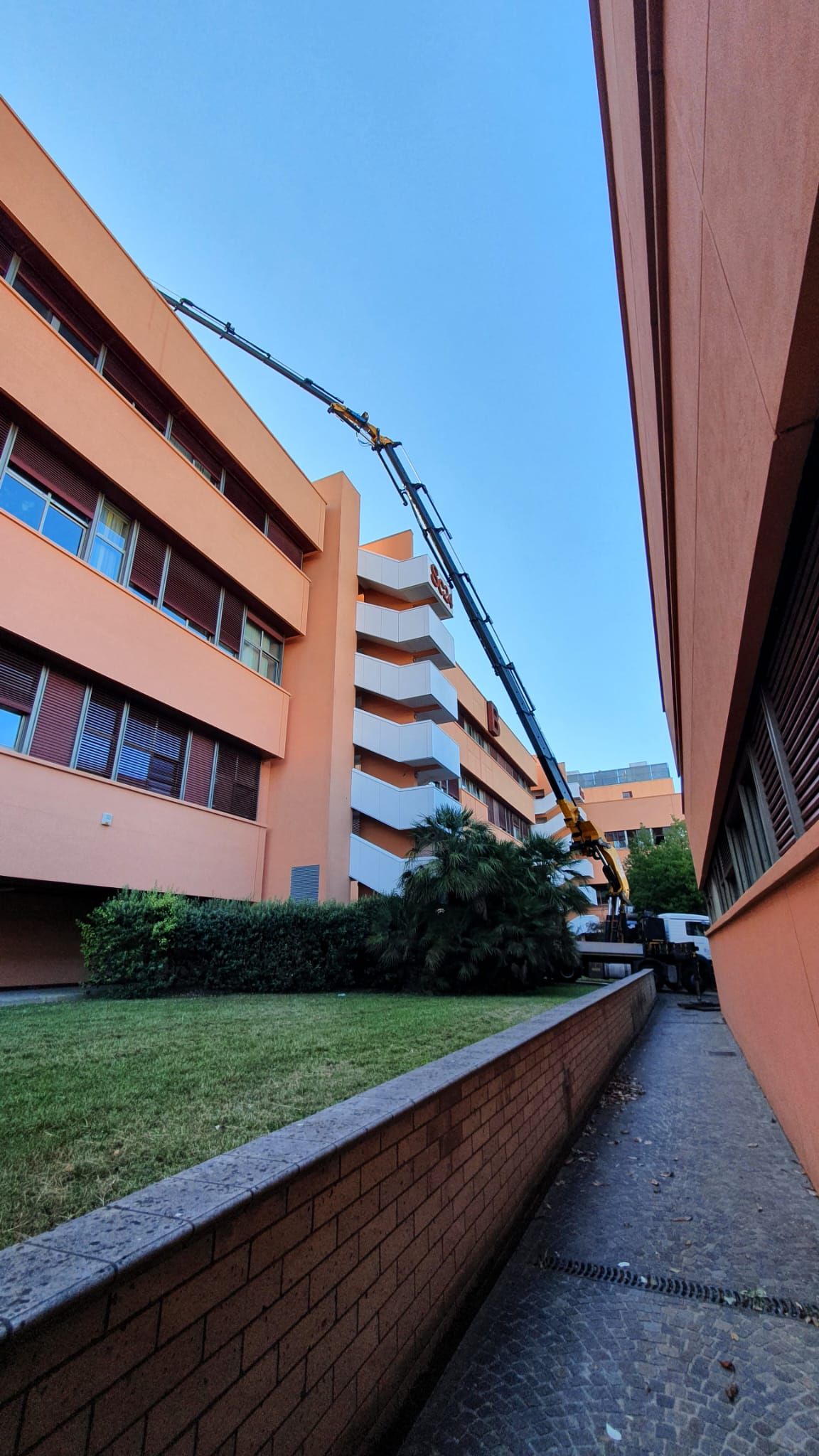 Stretto passaggio pedonale tra palazzi color pesca, sotto un cielo azzurro, con erba e muri di mattoni.