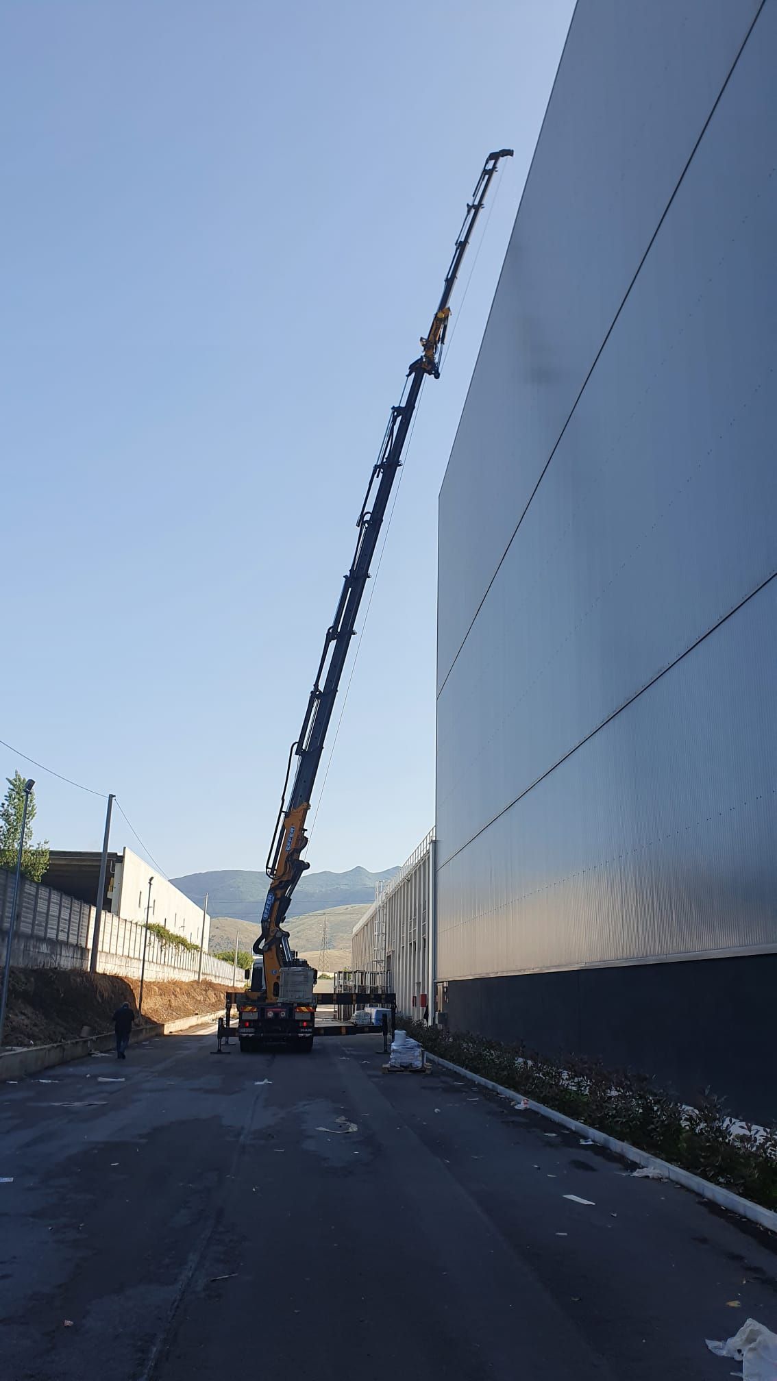 Una gru solleva materiali accanto a un alto edificio su una strada, con un altro edificio che si affaccia sul lato opposto.