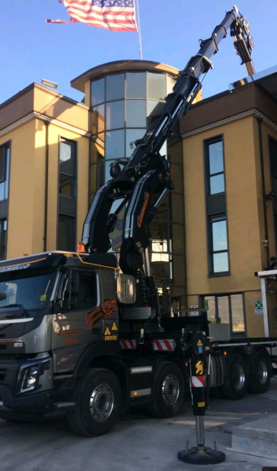 Un camion nero con il braccio della gru sollevato è parcheggiato accanto a un edificio in una strada cittadina.