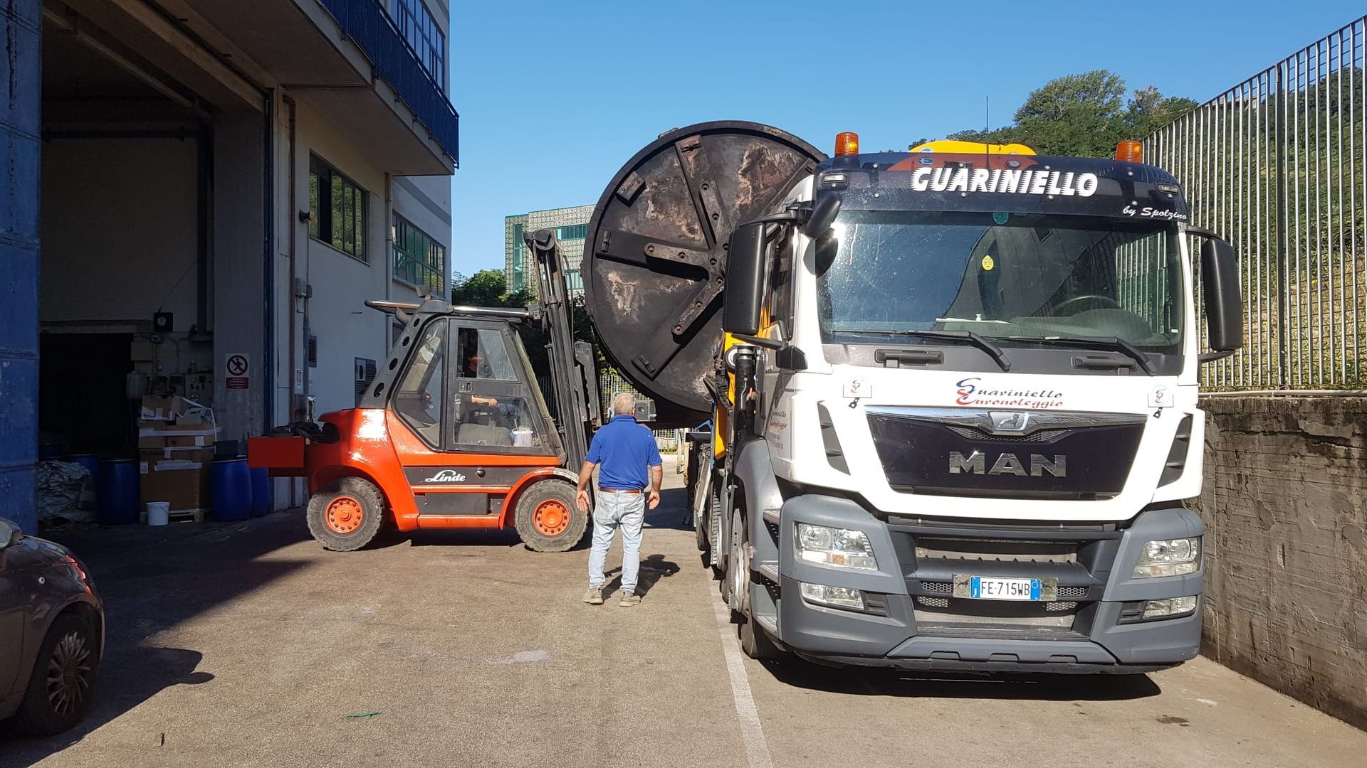 Due camion e un carrello elevatore in un cantiere, con un operaio in piedi accanto a un'autobetoniera.