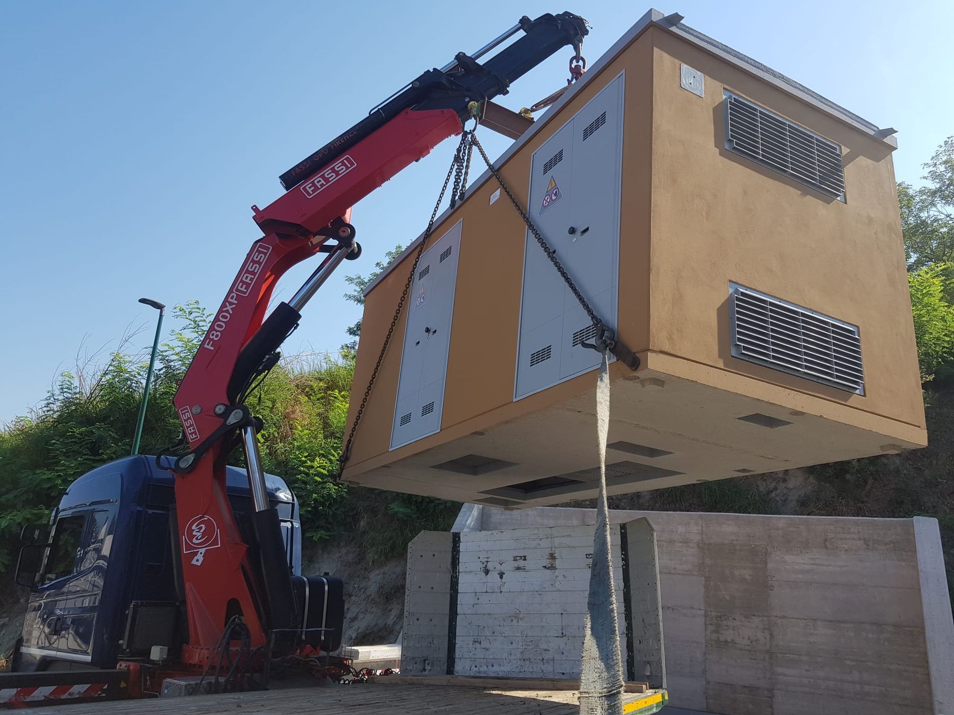 Una gru rossa solleva un piccolo modulo edilizio beige in un cantiere.