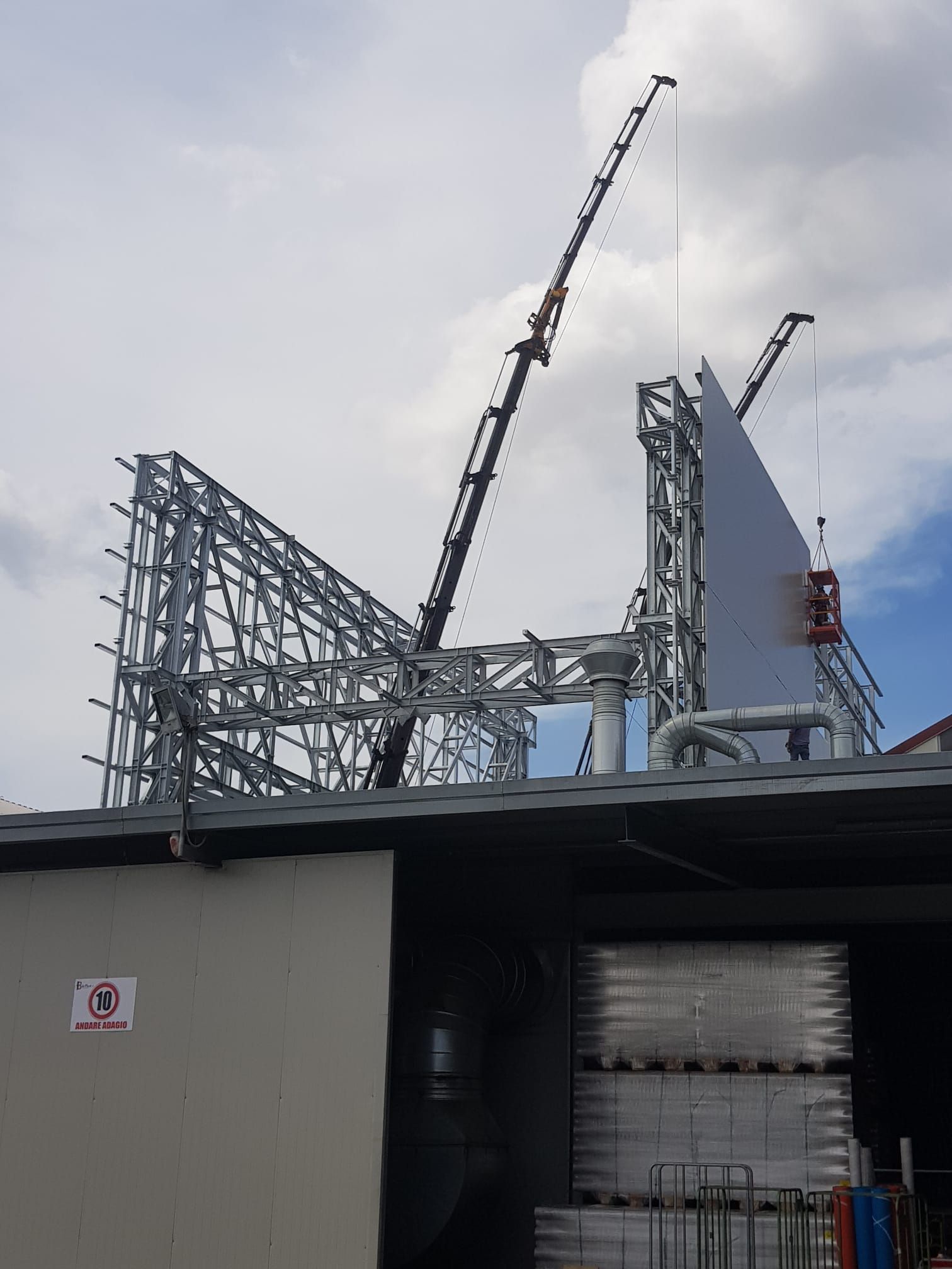 Struttura industriale in costruzione con gru e intelaiatura in acciaio sullo sfondo di un cielo nuvoloso.