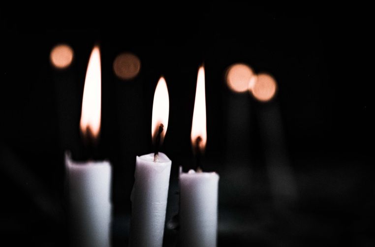 Three white memorial candles burning softly in a dark, peaceful setting.