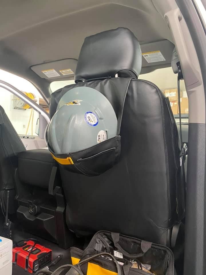Gray hard hat hanging on the back of a black car seat with safety gear in the back seat