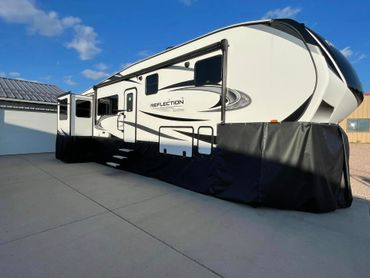 Large white travel trailer with black trim parked on a concrete driveway under a blue sky