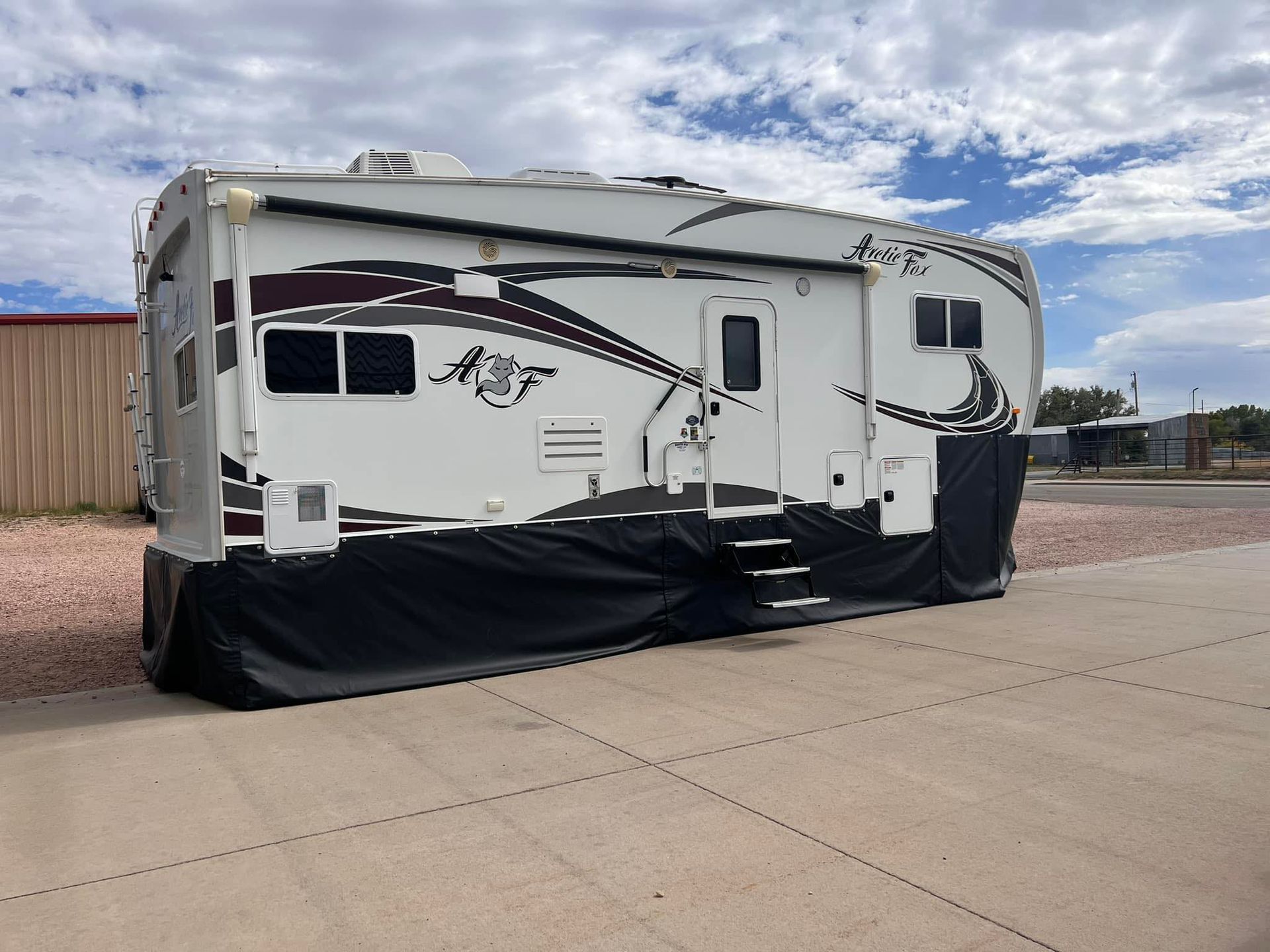 White RV with black lower skirting parked on a concrete lot under a cloudy sky.