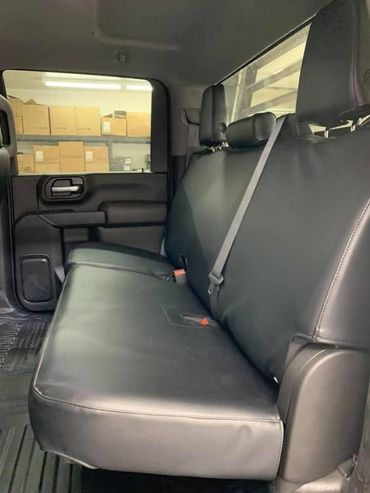 Black truck back seat with folding bench and cargo boxes visible through the rear side window