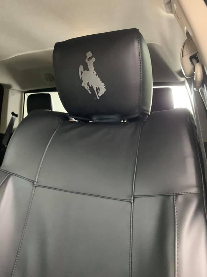 Black leather car seat with a headrest embroidered with a white cowboy silhouette.