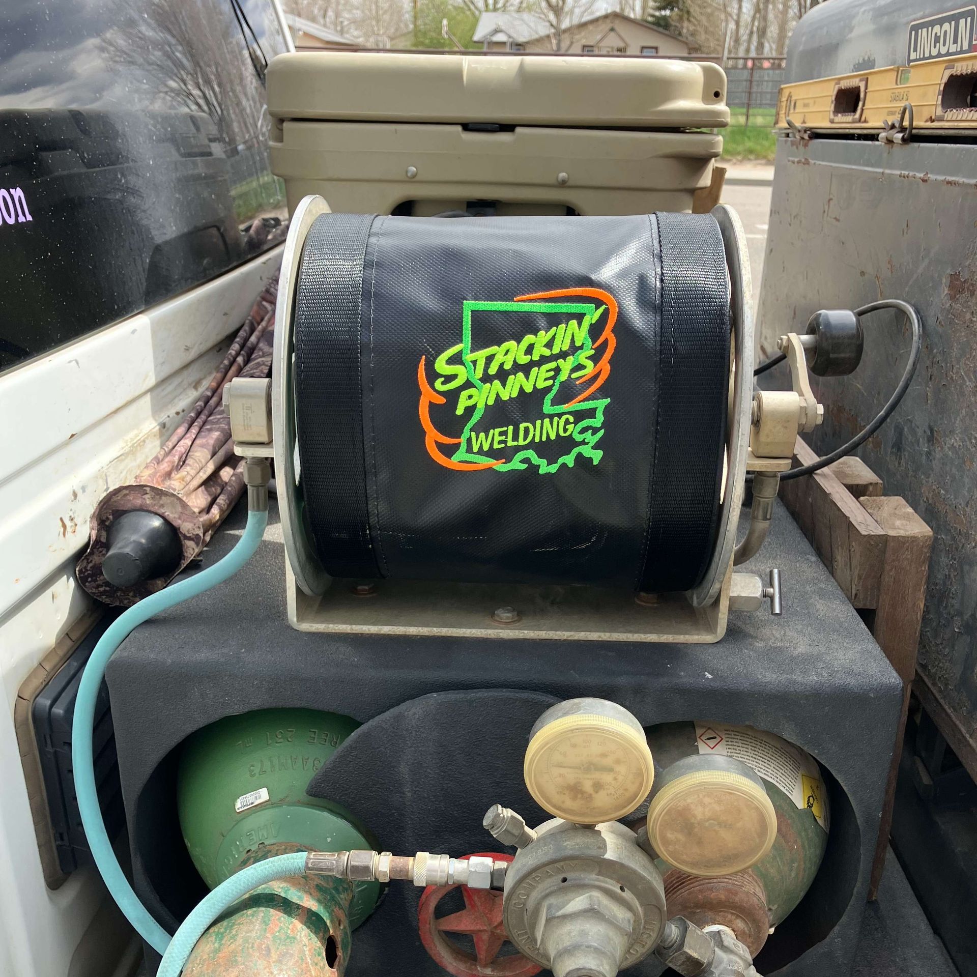 Small welding equipment setup with hoses, gauges, and a black “Stackin’ Fire Welding” spool on a trailer.
