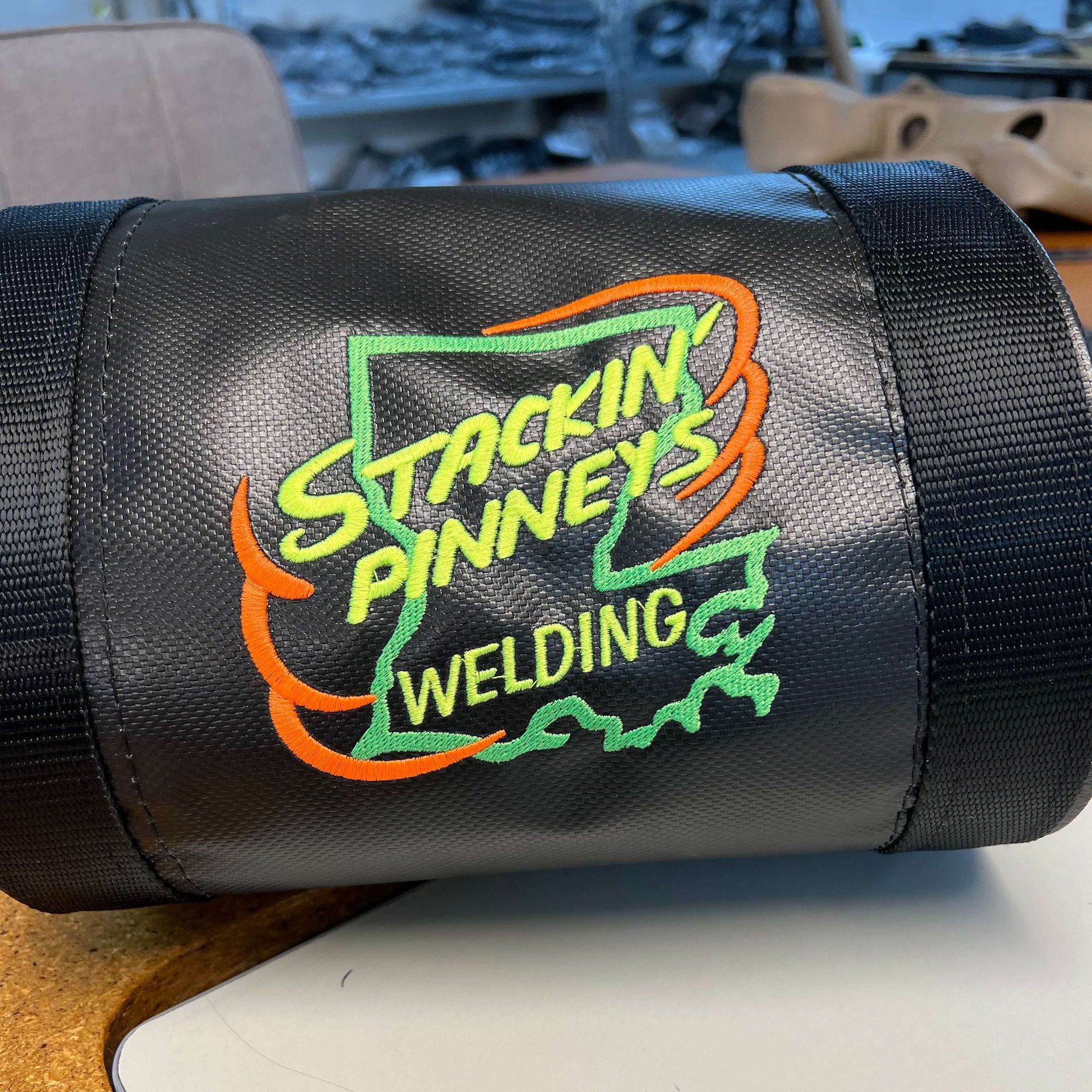 Black welding sleeve with neon green and orange “Stackin’ Pennies Welding” logo.