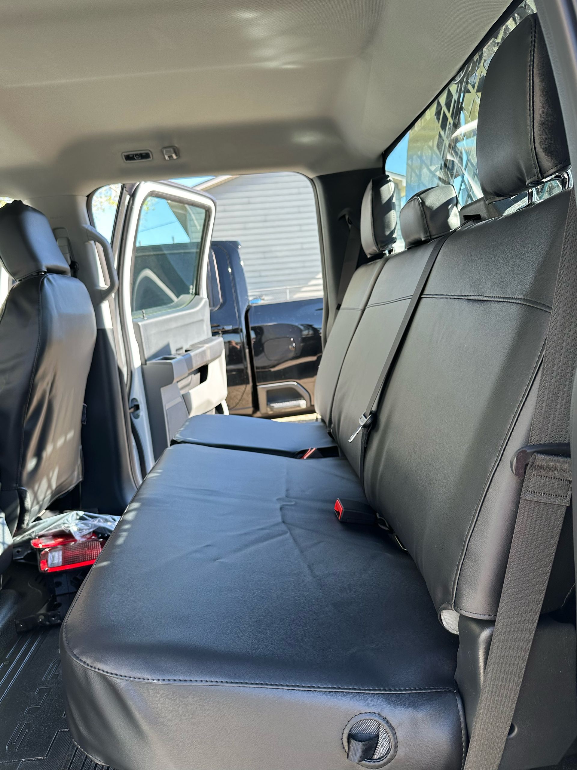 Van interior with black bench seat and an open side door, showing a blue tarp outside.