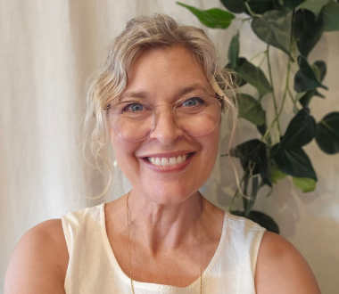 A woman in a white shirt is smiling in front of a tree.