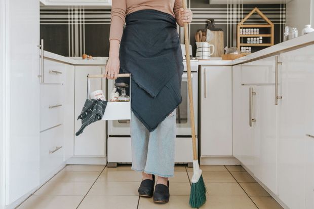 Person wearing an apron standing in a bright kitchen holding cleaning tools