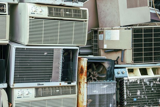 Stacked window air conditioners outdoors, with metal grilles and some rust and wear.