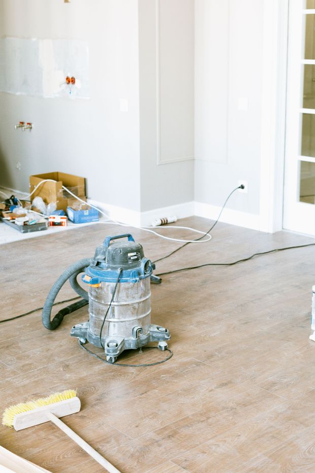 Dusty room with a vacuum sander on the floor and a broom nearby, suggesting renovation work