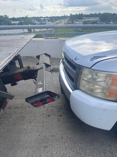 A silver car being towed by a blue tow truck on asphalt. A silver car being towed by a blue tow truck on asphalt.