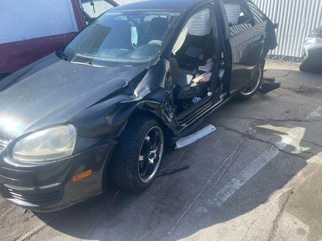 Black car, heavily damaged from a crash, parked outside. Airbags deployed, door ajar.