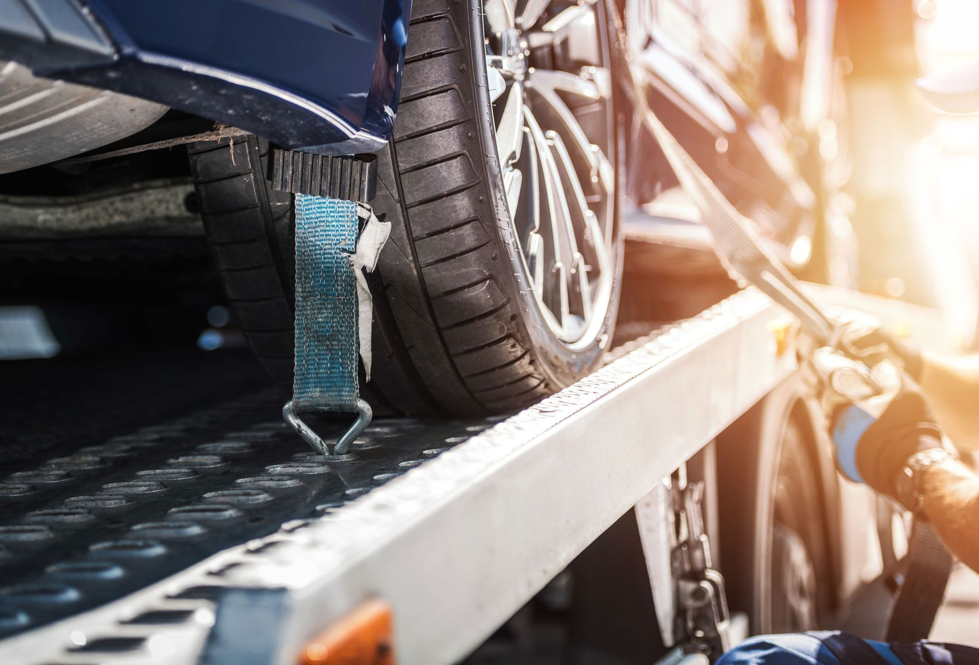 Blue car being secured with straps on a tow truck; sunlight.