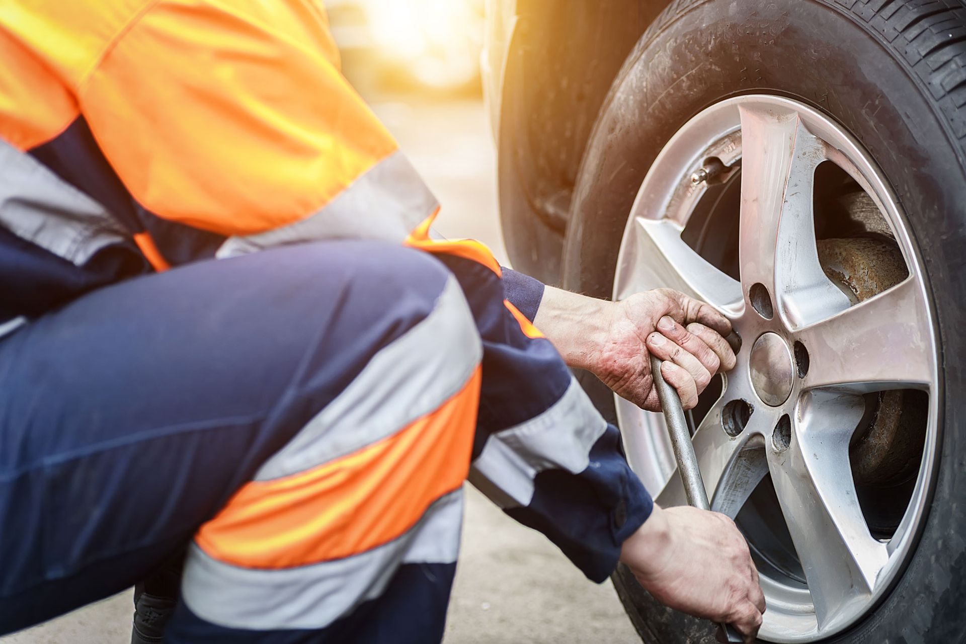 Mechanic in blue and orange overalls using a wrench to remove a car tire in an outdoor setting. Mechanic in blue and orange overalls using a wrench to remove a car tire in an outdoor setting.
