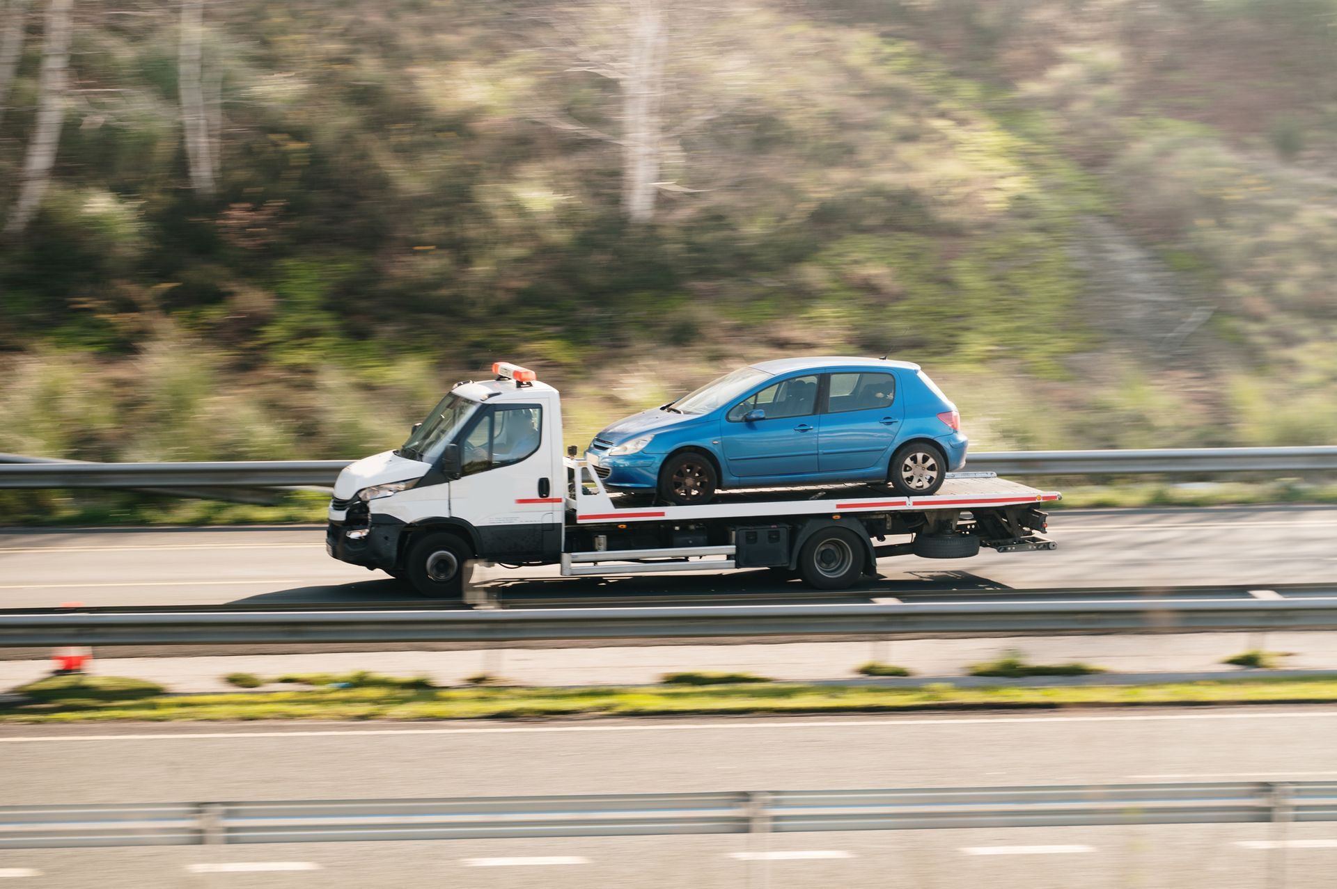 A blue car being transported on a flatbed tow truck along a highway.
