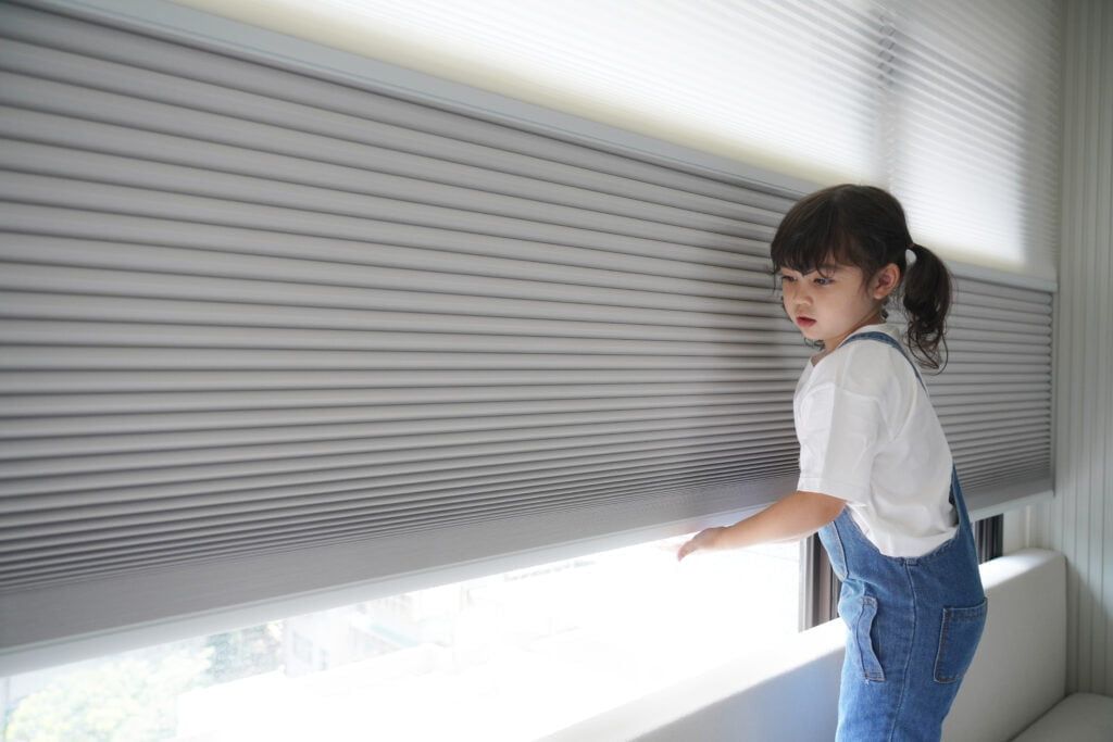 A Little Girl is Standing in Front of a Window Looking Out — TT Shutters & Shading In Ballina, NSW