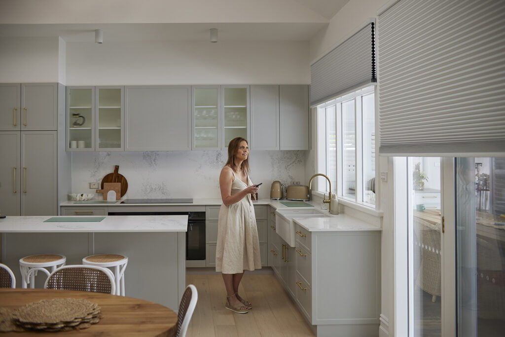A Woman is Standing in a Kitchen Looking at Her Phone — TT Shutters & Shading In Ballina, NSW