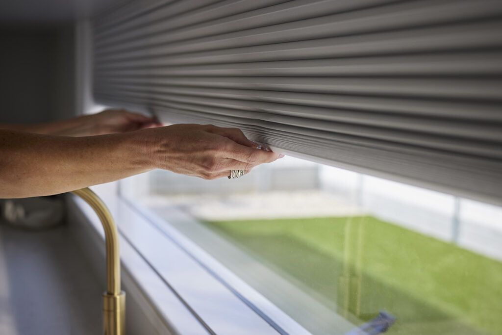 A Person is Opening a Roller Shutter on a Window — TT Shutters & Shading In Ballina, NSW