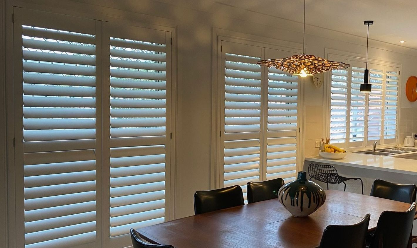 Dining room with wood table, black chairs, white shutters, and decorative lights.