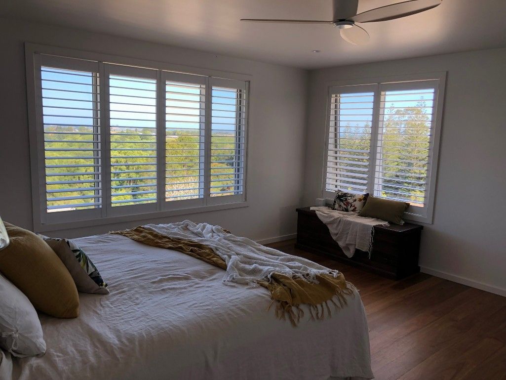 A Bedroom With A Bed, Ceiling Fan, And Shutters On The Windows — TT Shutters & Shading In Ballina, NSW