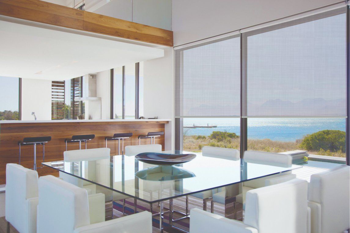 A Dining Room With a Glass Table and White Chairs and a View of the Ocean — TT Shutters & Shading In Ballina, NSW