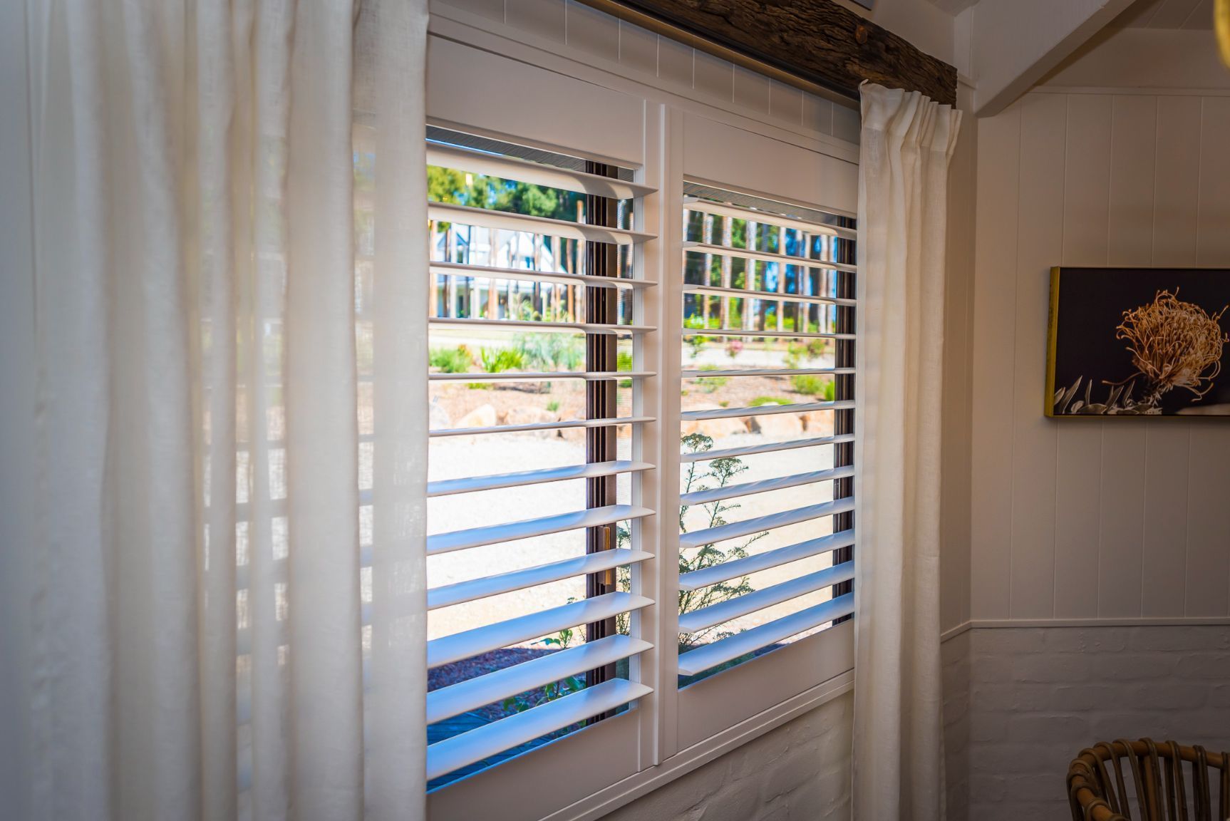 A Window With White Shutters And White Curtains In A Room — TT Shutters & Shading In Ballina, NSW