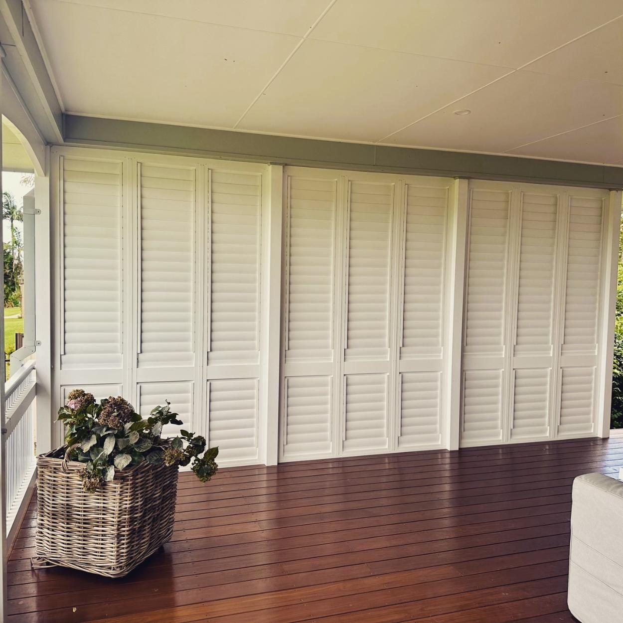 A Wicker Basket is Sitting on a Wooden Floor in a Room With White Shutters — TT Shutters & Shading In Ocean Shores, NSW